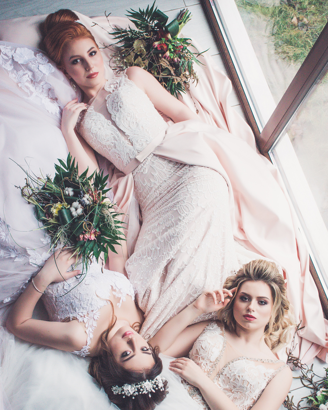 Three brides laying down next to each other in white wedding dresses and bouqet of flowers.